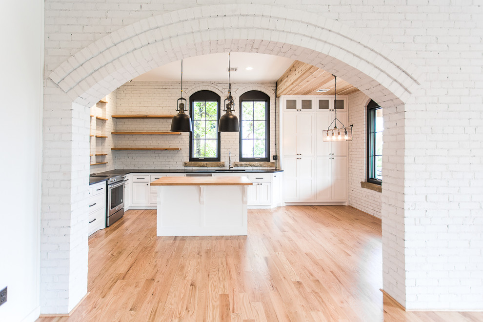This is an example of a medium sized traditional l-shaped kitchen/diner in Other with a submerged sink, shaker cabinets, white cabinets, granite worktops, white splashback, brick splashback, stainless steel appliances, light hardwood flooring, an island, red floors and black worktops.