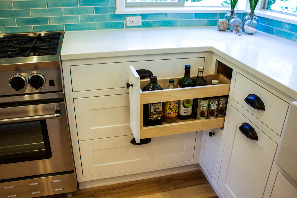 Example of a mid-sized beach style u-shaped medium tone wood floor open concept kitchen design in Portland with a farmhouse sink, shaker cabinets, white cabinets, quartz countertops, blue backsplash, subway tile backsplash, stainless steel appliances and an island