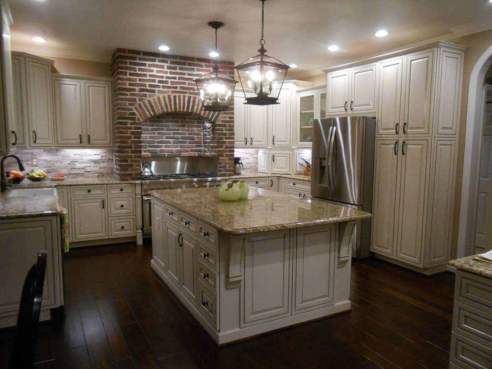 Klassisk inredning av ett stort kök, med luckor med upphöjd panel, granitbänkskiva, beige stänkskydd, stänkskydd i stenkakel, rostfria vitvaror, mörkt trägolv, en rustik diskho, vita skåp och en köksö