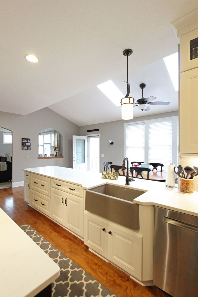 Large transitional l-shaped eat-in kitchen photo in Cleveland with a farmhouse sink, raised-panel cabinets, white cabinets, quartz countertops, gray backsplash, mosaic tile backsplash, stainless steel appliances, an island and white countertops