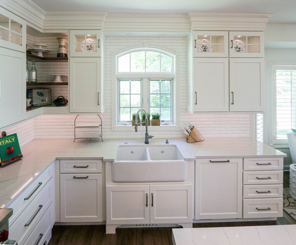Design ideas for a large classic u-shaped kitchen/diner in Cleveland with a belfast sink, flat-panel cabinets, white cabinets, engineered stone countertops, white splashback, ceramic splashback, white appliances, dark hardwood flooring, an island, brown floors and grey worktops.