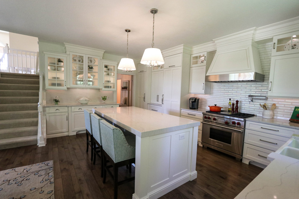 Bild på ett stort vintage grå grått kök, med en rustik diskho, släta luckor, vita skåp, bänkskiva i kvarts, vitt stänkskydd, stänkskydd i keramik, vita vitvaror, mörkt trägolv, en köksö och brunt golv