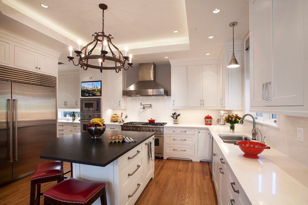 Example of a large classic l-shaped medium tone wood floor enclosed kitchen design in Houston with an undermount sink, recessed-panel cabinets, white cabinets, quartz countertops, white backsplash, stone slab backsplash, stainless steel appliances and an island