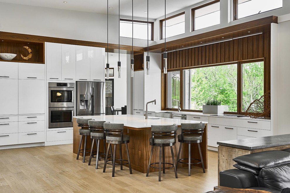 Photo of a large contemporary l-shaped open plan kitchen in Other with flat-panel cabinets, white cabinets, engineered stone countertops, stainless steel appliances, light hardwood flooring, an island, beige floors, a belfast sink, window splashback and white worktops.