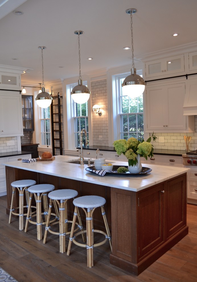 Mid-sized transitional u-shaped medium tone wood floor kitchen photo in Boston with an undermount sink, recessed-panel cabinets, white cabinets, solid surface countertops, white backsplash, subway tile backsplash, paneled appliances and an island
