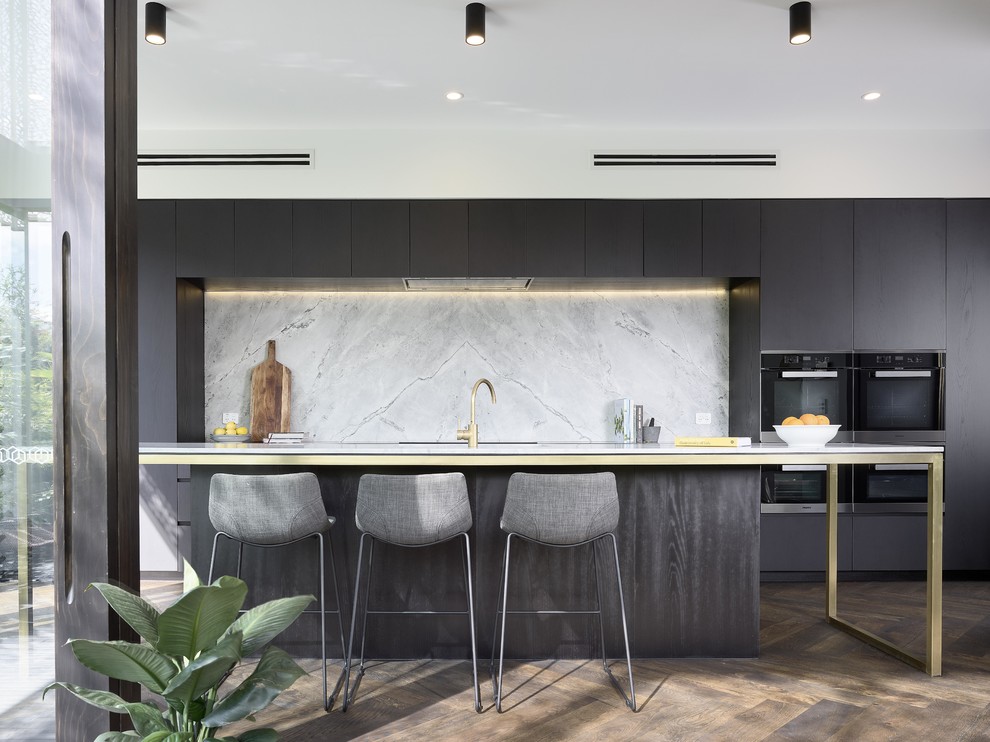 Zweizeilige Moderne Küche mit flächenbündigen Schrankfronten, grauen Schränken, Küchenrückwand in Grau, schwarzen Elektrogeräten, dunklem Holzboden, Kücheninsel, braunem Boden und weißer Arbeitsplatte in Brisbane