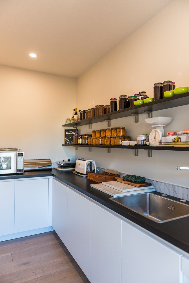Mid-sized trendy galley light wood floor and brown floor kitchen pantry photo in Christchurch with an undermount sink, flat-panel cabinets, yellow cabinets, quartz countertops, green backsplash, glass sheet backsplash, stainless steel appliances and an island
