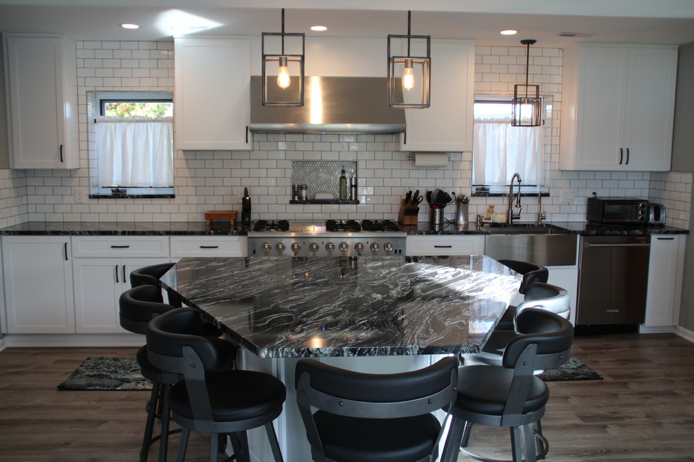 Mid-sized beach style l-shaped vinyl floor and gray floor eat-in kitchen photo in Detroit with a farmhouse sink, shaker cabinets, white cabinets, granite countertops, white backsplash, ceramic backsplash, stainless steel appliances, an island and black countertops