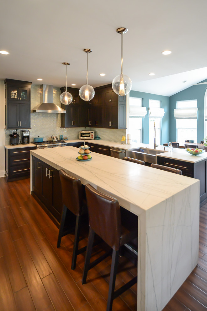 Example of a mid-sized trendy l-shaped medium tone wood floor eat-in kitchen design in Philadelphia with a farmhouse sink, shaker cabinets, dark wood cabinets, quartzite countertops, glass tile backsplash, stainless steel appliances and an island