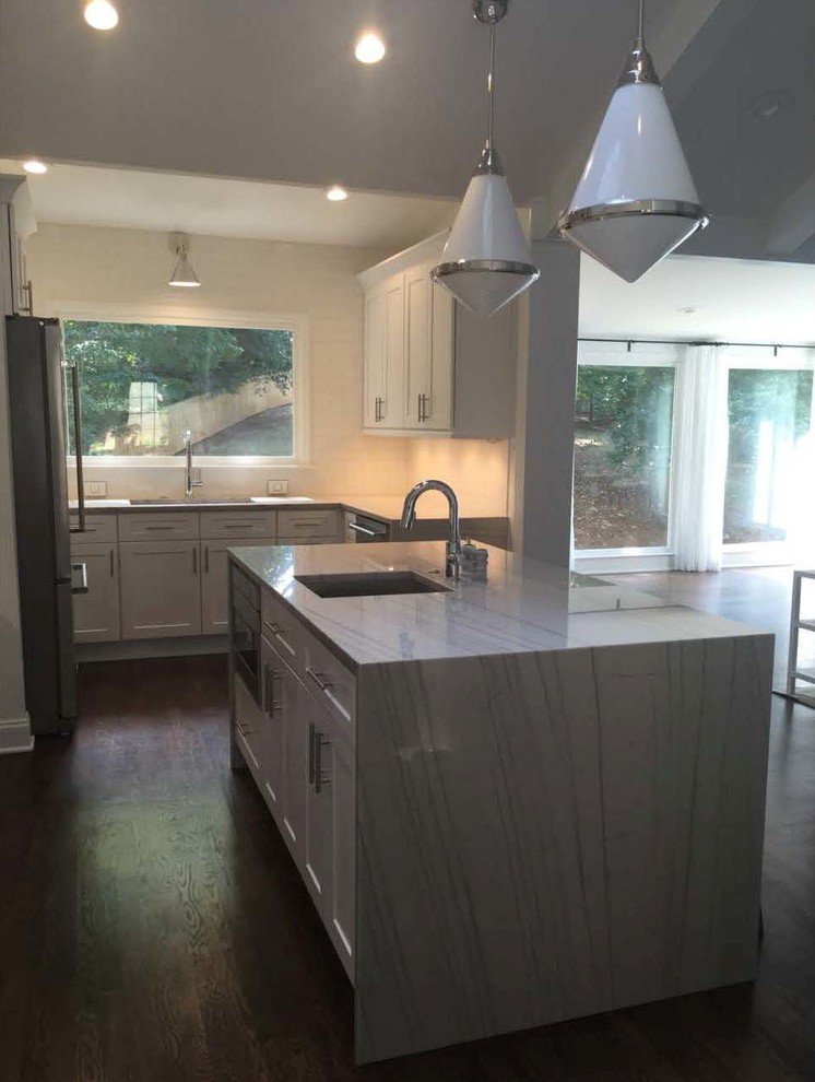 Example of a trendy l-shaped brown floor open concept kitchen design in Atlanta with glass-front cabinets, an island, an undermount sink, white cabinets, quartzite countertops, white backsplash, subway tile backsplash and stainless steel appliances