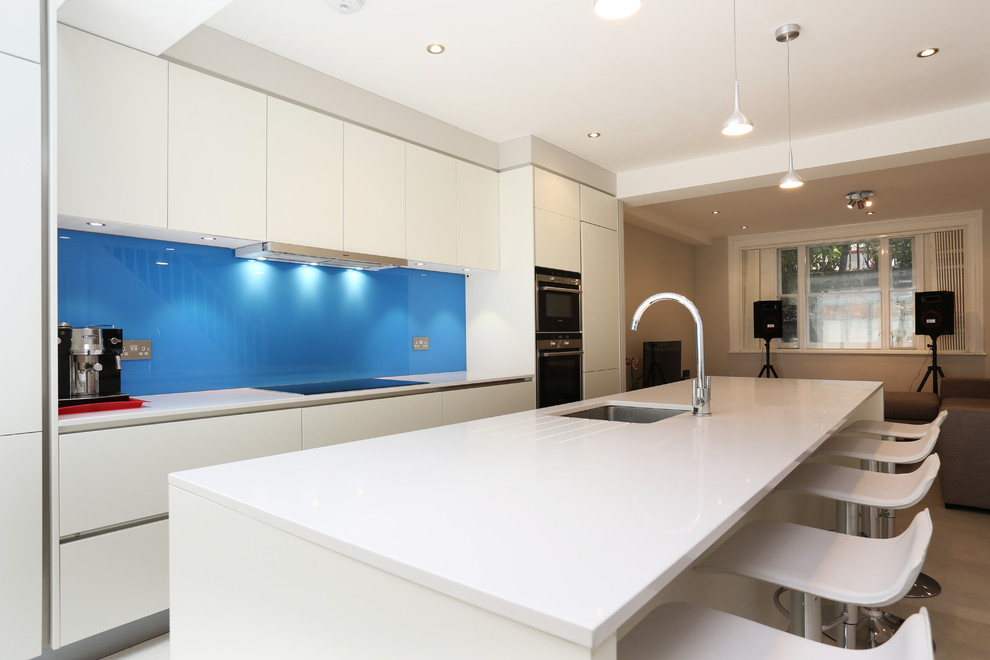 Esempio di una cucina minimalista con ante lisce, ante bianche, paraspruzzi blu, paraspruzzi con lastra di vetro, elettrodomestici in acciaio inossidabile e pavimento in gres porcellanato