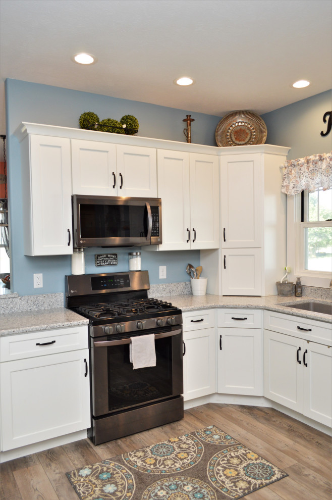Foto på ett stort lantligt grå kök, med en undermonterad diskho, skåp i shakerstil, vita skåp, bänkskiva i kvartsit, rostfria vitvaror, laminatgolv, en halv köksö och brunt golv