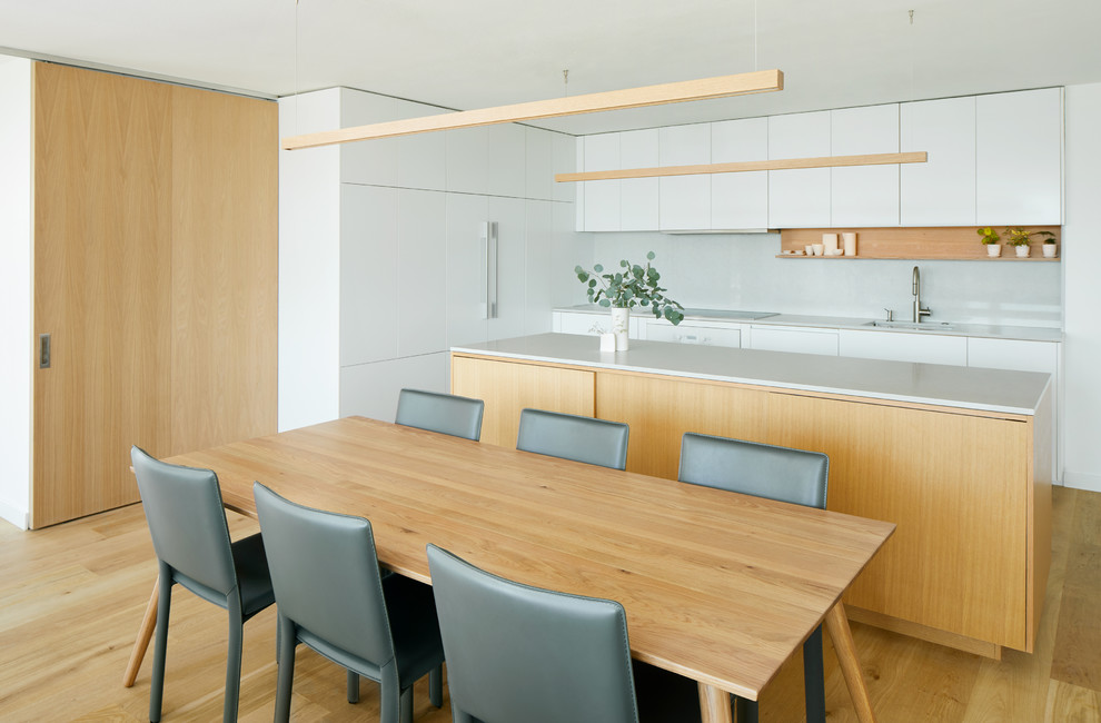 Inredning av ett minimalistiskt mellanstort grå grått kök och matrum, med en undermonterad diskho, släta luckor, vita skåp, bänkskiva i kvarts, grått stänkskydd, ljust trägolv, en köksö och integrerade vitvaror
