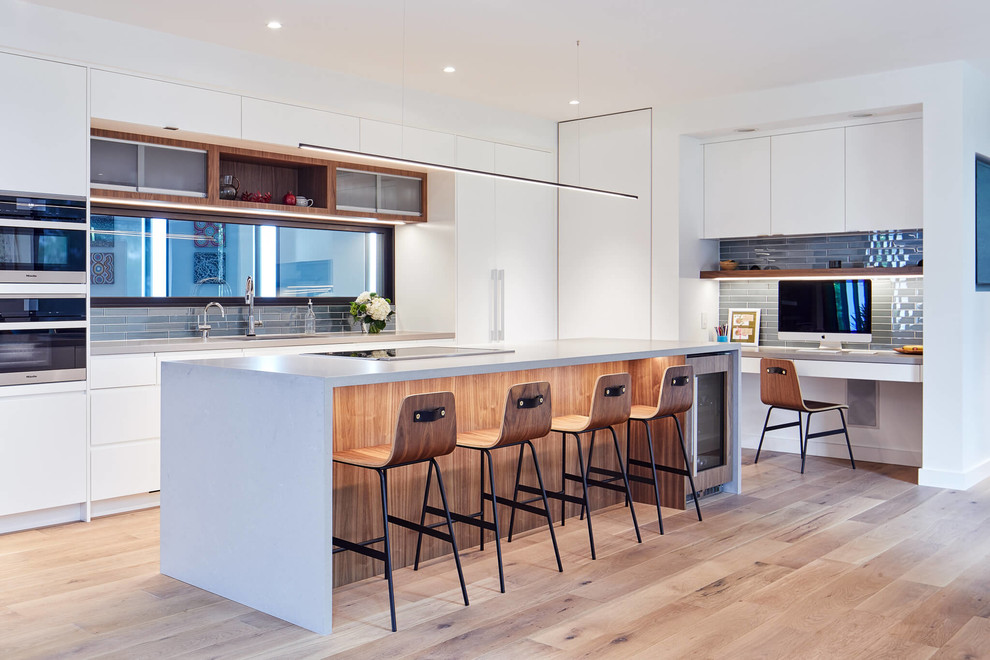 Photo of a contemporary kitchen in Ottawa with flat-panel cabinets, white cabinets, grey splashback, glass tiled splashback, light hardwood flooring, an island, beige floors and grey worktops.