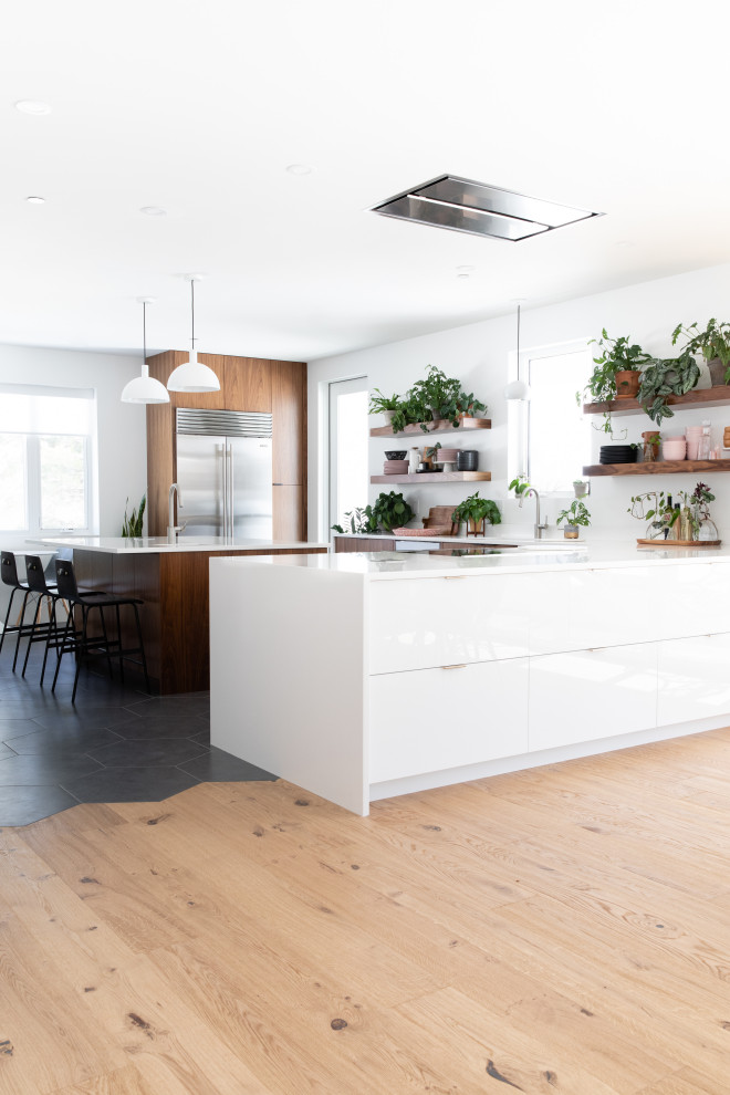 Aménagement d'une cuisine ouverte contemporaine en L et bois brun avec un placard à porte plane, un électroménager en acier inoxydable, îlot, un sol noir et un plan de travail blanc.