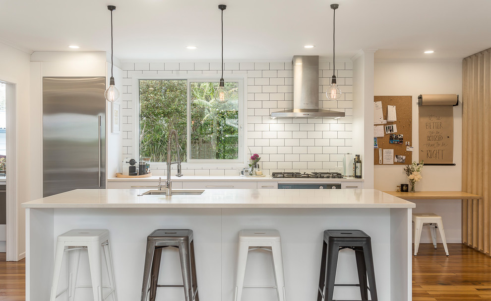 Mid-sized trendy single-wall light wood floor and beige floor open concept kitchen photo in Auckland with an undermount sink, flat-panel cabinets, white cabinets, quartz countertops, white backsplash, subway tile backsplash, stainless steel appliances, an island and white countertops
