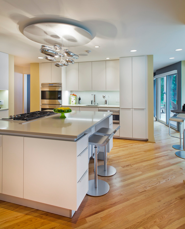 Example of a large trendy u-shaped medium tone wood floor eat-in kitchen design in Minneapolis with an undermount sink, flat-panel cabinets, white cabinets, quartz countertops, white backsplash, glass sheet backsplash, paneled appliances and an island