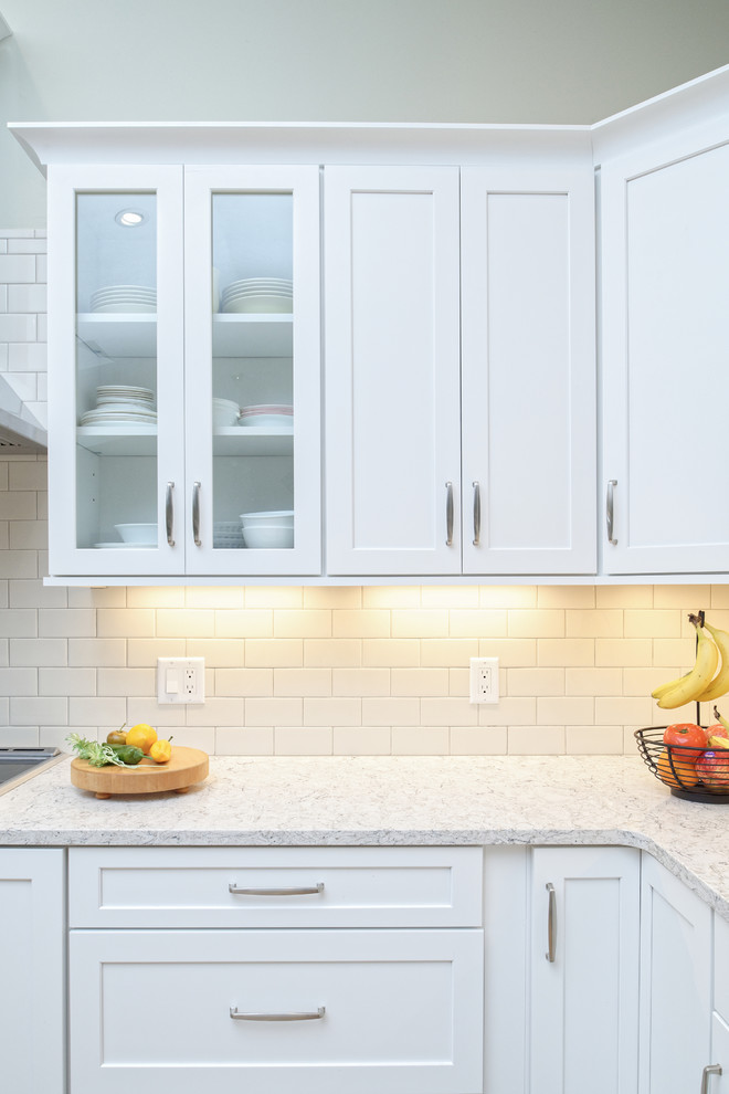 Bild på ett mellanstort funkis kök, med en undermonterad diskho, skåp i shakerstil, vita skåp, bänkskiva i kvarts, vitt stänkskydd, stänkskydd i tunnelbanekakel, rostfria vitvaror, mellanmörkt trägolv, en köksö och orange golv