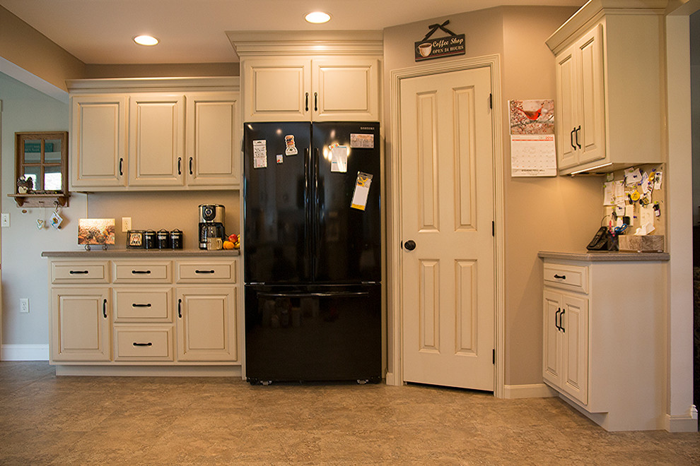 Example of a mid-sized classic l-shaped eat-in kitchen design in Philadelphia with a double-bowl sink, raised-panel cabinets, white cabinets, laminate countertops, black appliances and no island