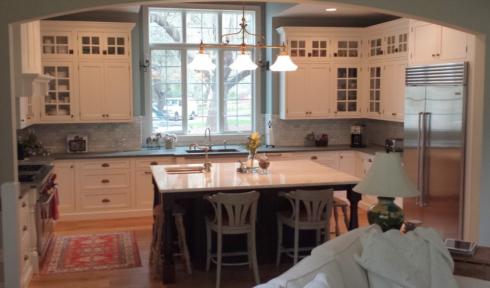 Klassisk inredning av ett u-kök, med en dubbel diskho, luckor med profilerade fronter, vita skåp, granitbänkskiva, flerfärgad stänkskydd, stänkskydd i stenkakel, rostfria vitvaror och mellanmörkt trägolv