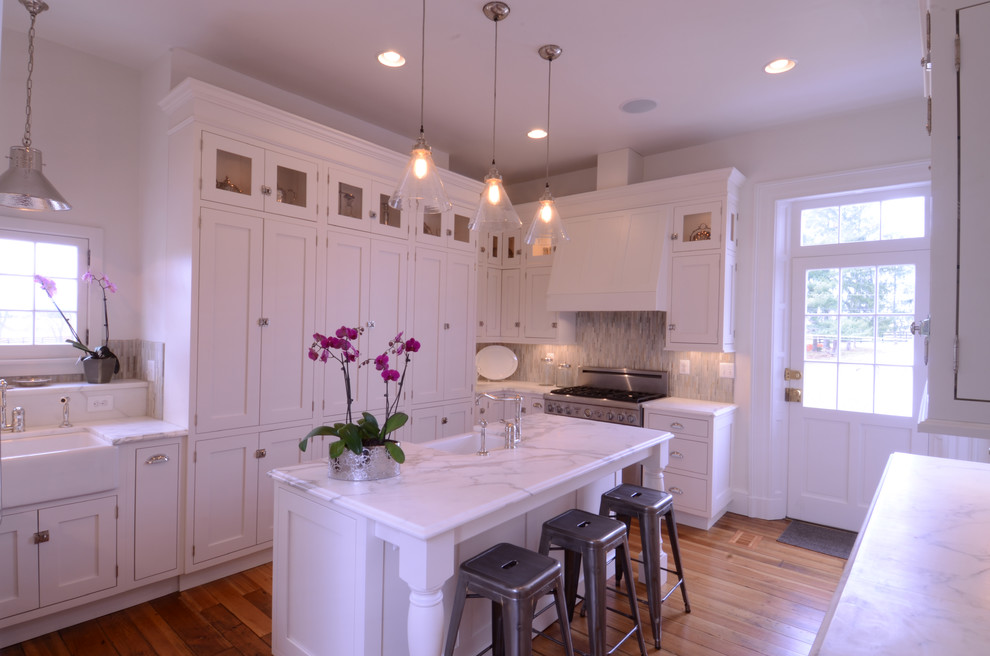 Large elegant u-shaped medium tone wood floor and brown floor eat-in kitchen photo in Baltimore with a farmhouse sink, shaker cabinets, white cabinets, marble countertops, gray backsplash, stone tile backsplash, paneled appliances and an island