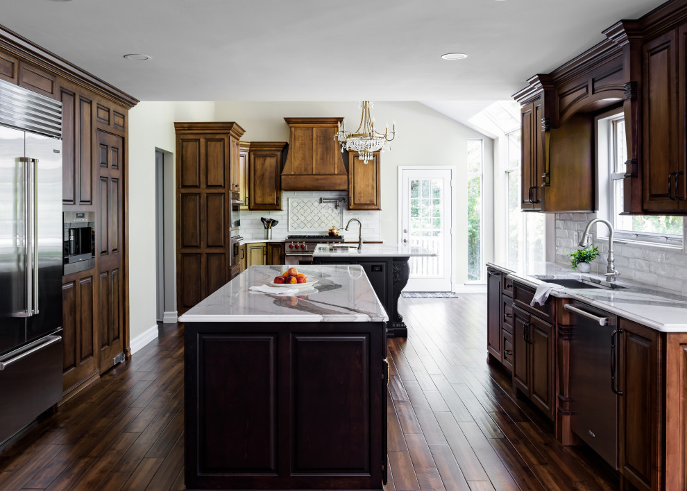 Large elegant brown floor kitchen photo in St Louis with a drop-in sink, raised-panel cabinets, medium tone wood cabinets, quartz countertops, white backsplash, subway tile backsplash, stainless steel appliances, two islands and white countertops