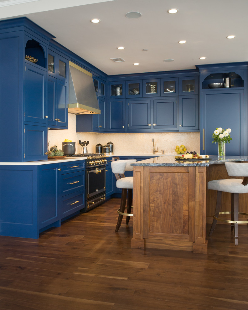 Example of a mid-sized classic l-shaped medium tone wood floor eat-in kitchen design in New York with an undermount sink, recessed-panel cabinets, blue cabinets, granite countertops, beige backsplash, stone tile backsplash, black appliances and an island