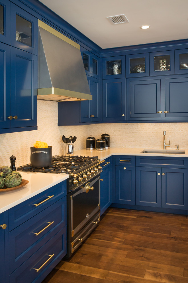 Inredning av ett klassiskt mellanstort kök, med en undermonterad diskho, luckor med infälld panel, blå skåp, granitbänkskiva, beige stänkskydd, stänkskydd i stenkakel, svarta vitvaror, mellanmörkt trägolv och en köksö