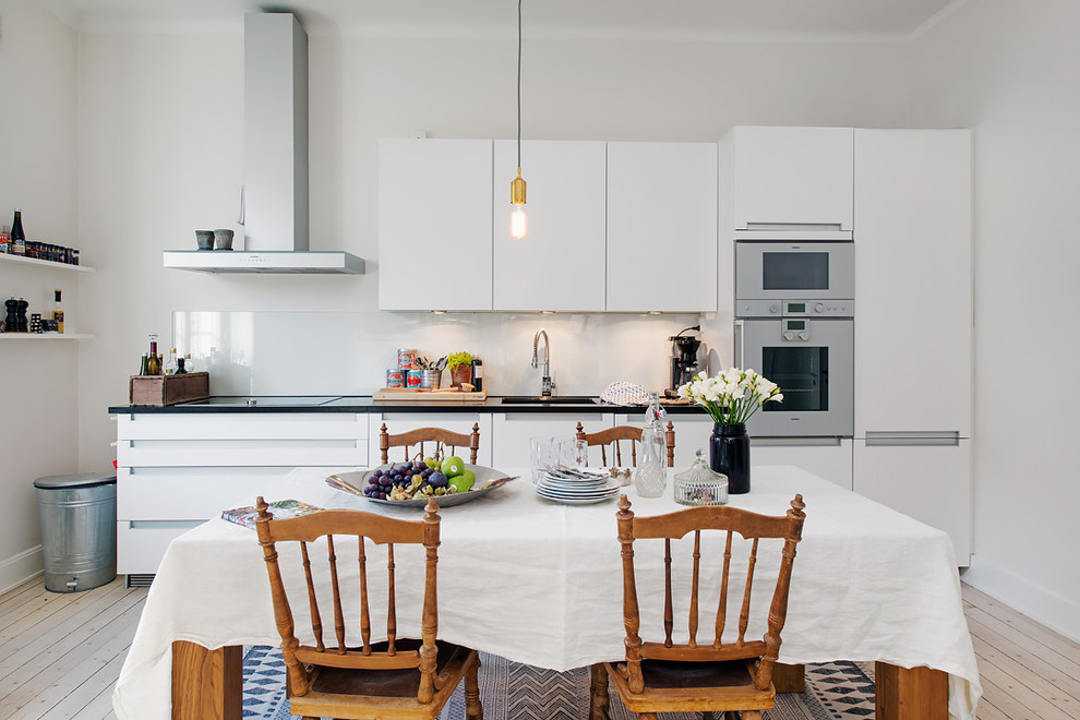 Photo of a scandi single-wall kitchen/diner in Stockholm with flat-panel cabinets, white cabinets, stainless steel appliances, light hardwood flooring, a submerged sink, no island and beige floors.