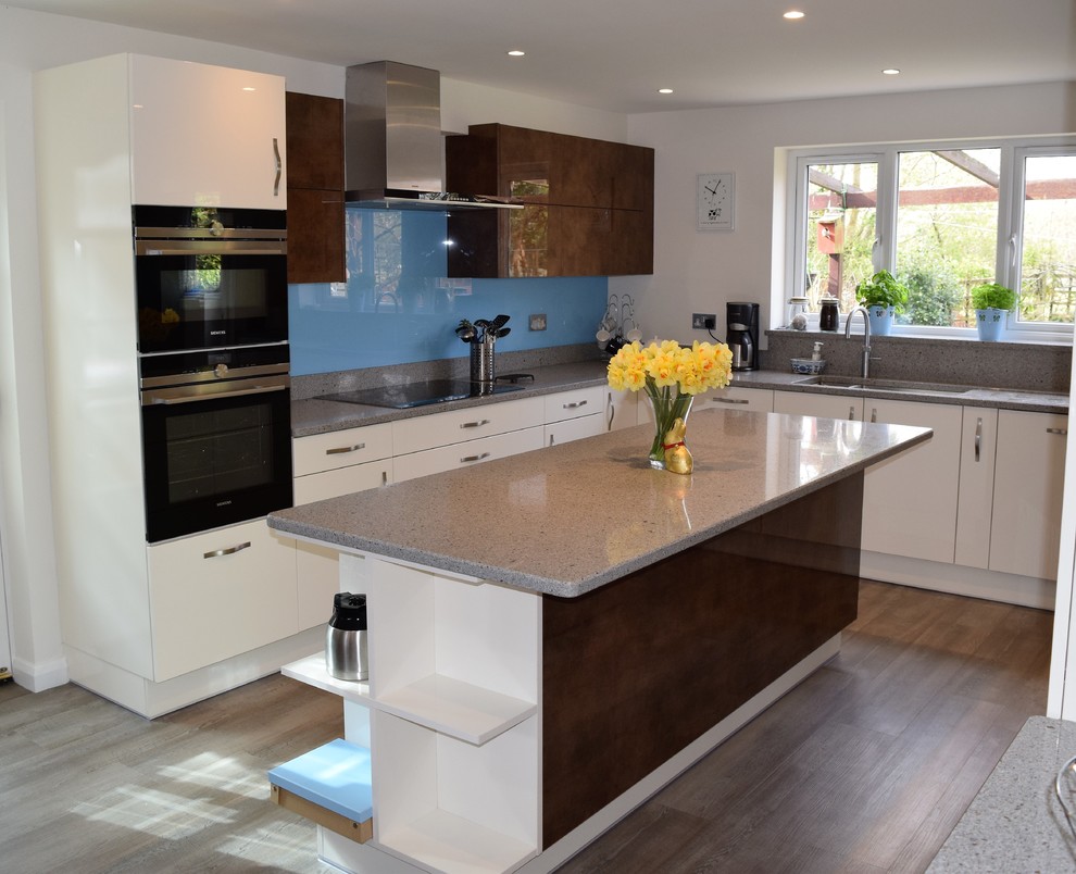 Inspiration for a medium sized contemporary kitchen/diner in Hampshire with white cabinets, engineered stone countertops, blue splashback, glass sheet splashback, black appliances, vinyl flooring and an island.