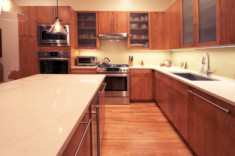 Inredning av ett modernt stort vit vitt kök, med en undermonterad diskho, släta luckor, skåp i mellenmörkt trä, bänkskiva i kvartsit, gult stänkskydd, stänkskydd i glaskakel, rostfria vitvaror, mellanmörkt trägolv, en köksö och brunt golv