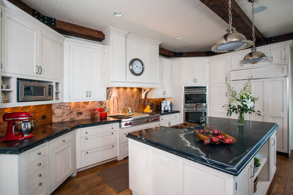 Example of a huge classic l-shaped medium tone wood floor eat-in kitchen design in Chicago with a double-bowl sink, recessed-panel cabinets, white cabinets, granite countertops, orange backsplash, stone slab backsplash, paneled appliances and an island