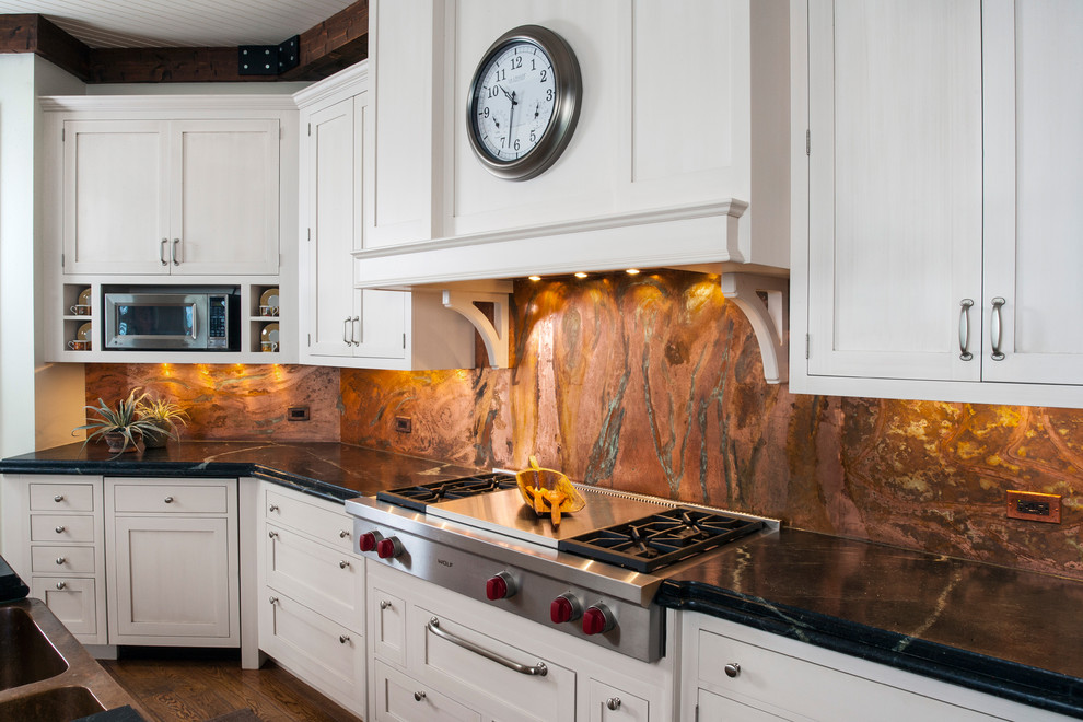 Inredning av ett klassiskt mycket stort l-kök, med en dubbel diskho, luckor med infälld panel, vita skåp, granitbänkskiva, orange stänkskydd, stänkskydd i sten, integrerade vitvaror, mellanmörkt trägolv och en köksö