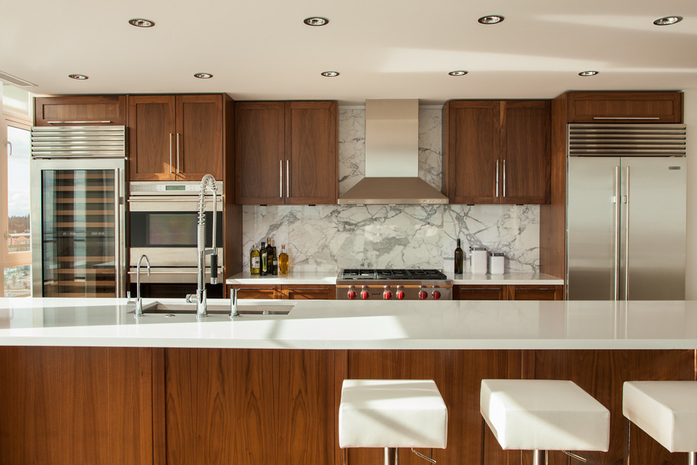Design ideas for a contemporary galley kitchen in Vancouver with recessed-panel cabinets, white splashback, stone slab splashback, stainless steel appliances and dark wood cabinets.