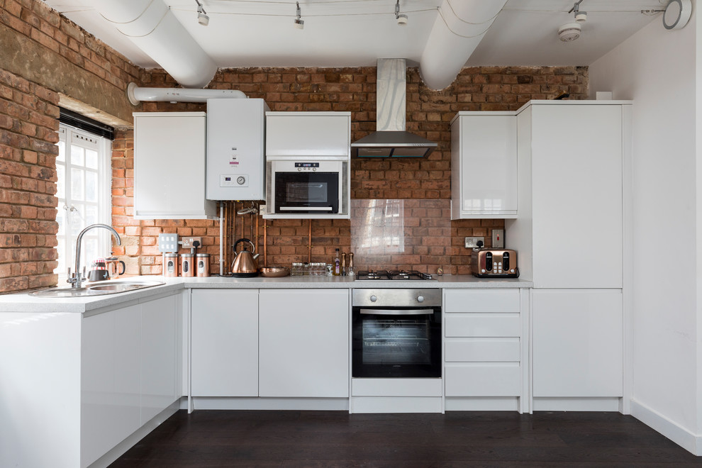 This is an example of a contemporary l-shaped kitchen in London with a built-in sink, flat-panel cabinets, white cabinets, red splashback, brick splashback, integrated appliances, dark hardwood flooring, no island, brown floors and grey worktops.