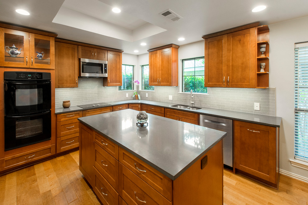 Foto på ett mellanstort amerikanskt kök, med en undermonterad diskho, släta luckor, skåp i mellenmörkt trä, bänkskiva i kvarts, beige stänkskydd, stänkskydd i glaskakel, svarta vitvaror, mellanmörkt trägolv, en köksö och brunt golv