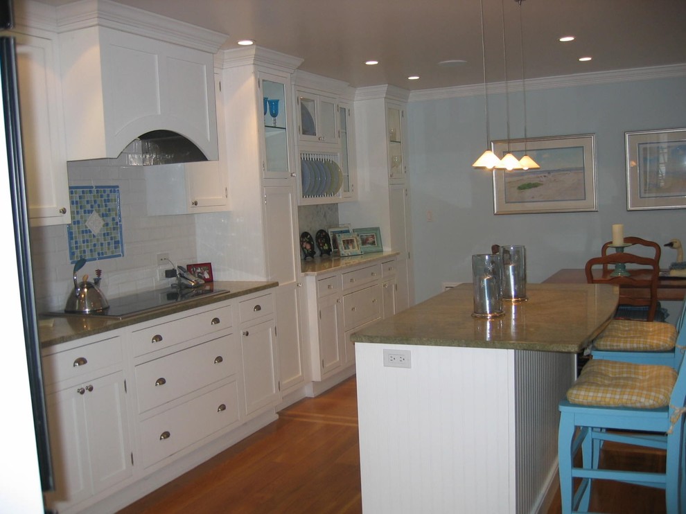 This is an example of a medium sized traditional l-shaped kitchen/diner in New York with a submerged sink, white cabinets, granite worktops, white splashback, metro tiled splashback, stainless steel appliances, medium hardwood flooring, an island and shaker cabinets.