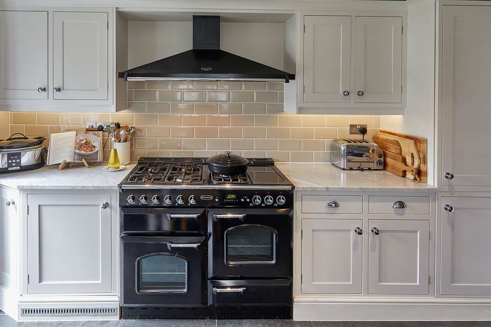 Klassisk inredning av ett mellanstort vit vitt kök, med en rustik diskho, skåp i shakerstil, vita skåp, marmorbänkskiva, beige stänkskydd, stänkskydd i porslinskakel, svarta vitvaror, skiffergolv och grått golv