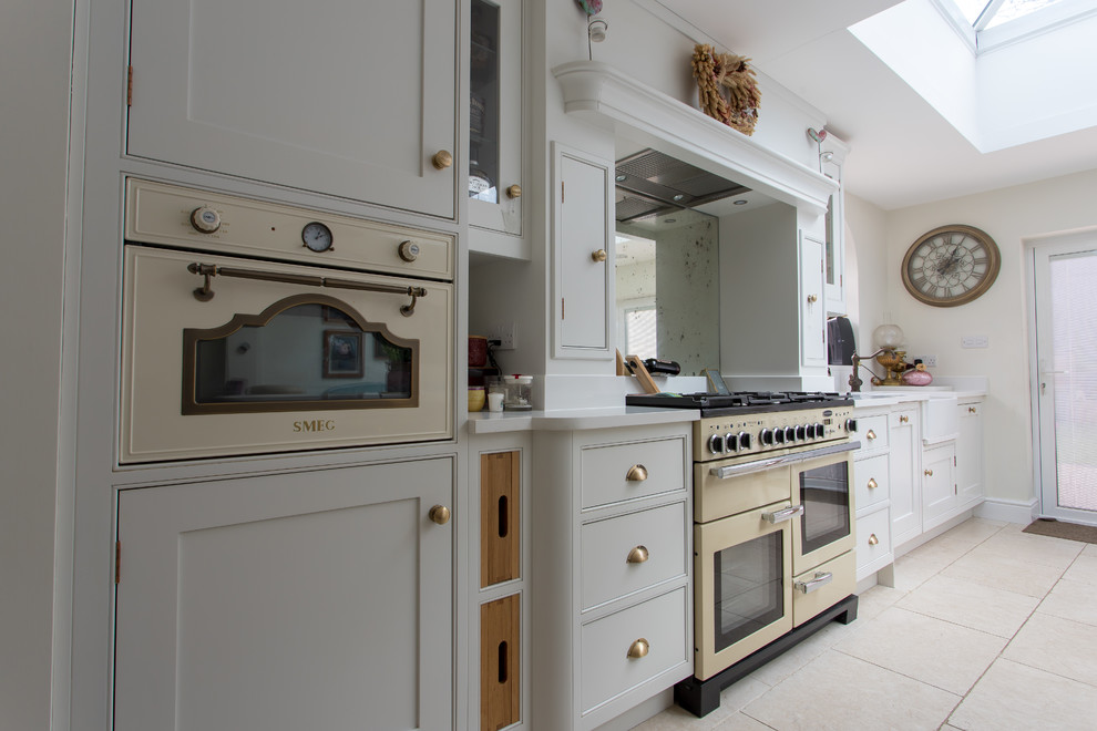 Example of a large classic l-shaped porcelain tile and beige floor eat-in kitchen design in Hertfordshire with a single-bowl sink, shaker cabinets, yellow cabinets, soapstone countertops, metallic backsplash, mirror backsplash, stainless steel appliances, an island and white countertops