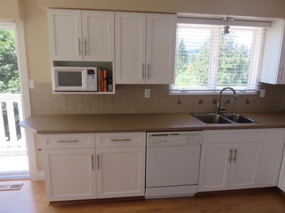Inspiration for a medium sized contemporary u-shaped enclosed kitchen in Vancouver with a built-in sink, shaker cabinets, white cabinets, laminate countertops, beige splashback, ceramic splashback, white appliances, light hardwood flooring and no island.