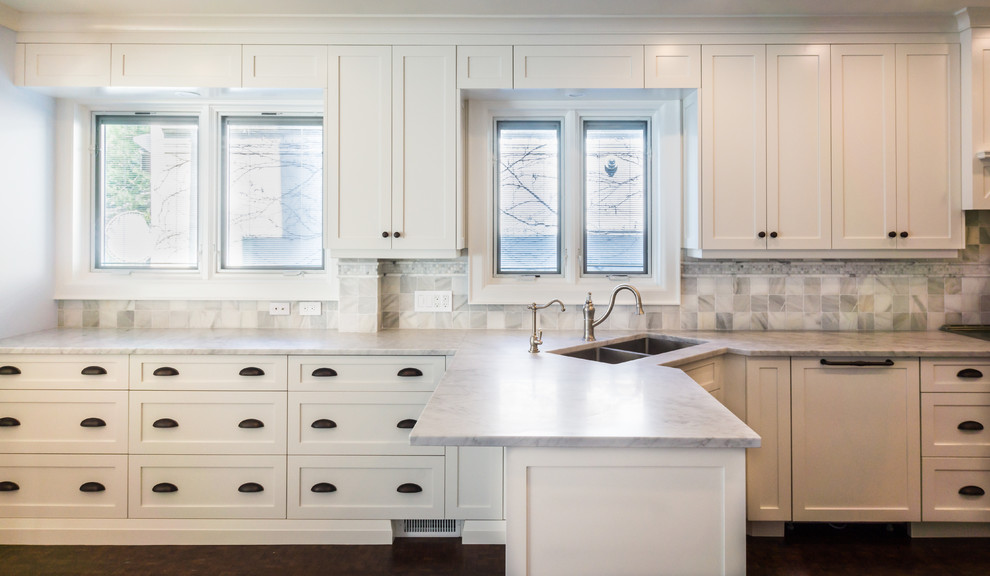 Large traditional u-shaped enclosed kitchen in Toronto with a submerged sink, shaker cabinets, white cabinets, marble worktops, white splashback, stone tiled splashback, stainless steel appliances, dark hardwood flooring, a breakfast bar and brown floors.