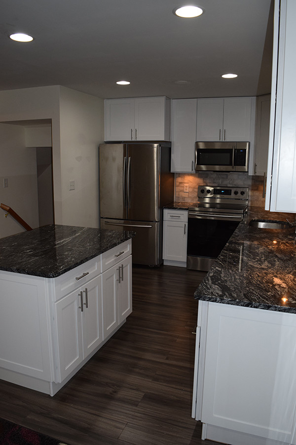 Example of a mid-sized trendy l-shaped laminate floor and brown floor eat-in kitchen design in DC Metro with an undermount sink, shaker cabinets, white cabinets, granite countertops, stainless steel appliances, an island, gray backsplash and stone tile backsplash