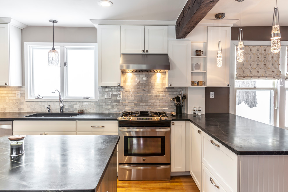 Mid-sized arts and crafts u-shaped light wood floor eat-in kitchen photo in Burlington with an undermount sink, shaker cabinets, white cabinets, soapstone countertops, white backsplash, stone tile backsplash, stainless steel appliances and an island