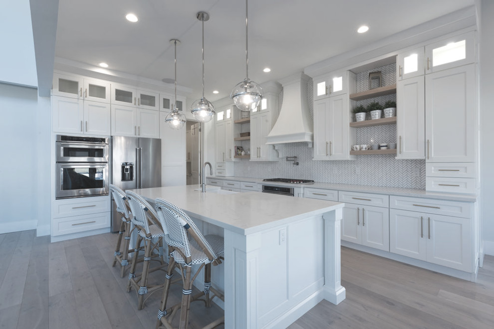 This is an example of an expansive country l-shaped kitchen/diner in Salt Lake City with shaker cabinets, white cabinets, multi-coloured splashback, stainless steel appliances, light hardwood flooring, an island, white worktops, engineered stone countertops and marble splashback.