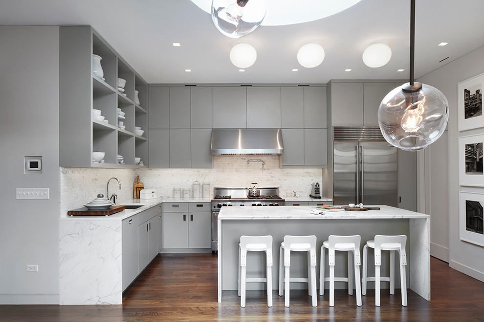 Example of a large minimalist l-shaped medium tone wood floor eat-in kitchen design in New York with an undermount sink, flat-panel cabinets, gray cabinets, marble countertops, white backsplash, stone tile backsplash, stainless steel appliances and an island