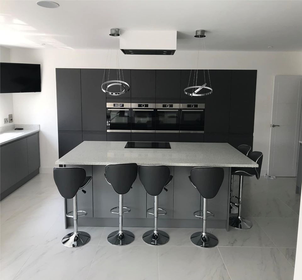 Einzeilige Moderne Küche mit schwarzen Schränken, Quarzit-Arbeitsplatte, Elektrogeräten mit Frontblende, Kücheninsel und weißer Arbeitsplatte in West Midlands