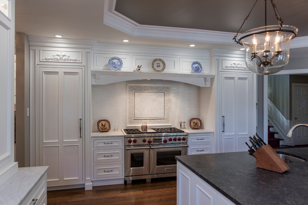 Inredning av ett klassiskt stort kök, med en rustik diskho, luckor med infälld panel, vita skåp, marmorbänkskiva, vitt stänkskydd, stänkskydd i keramik, integrerade vitvaror, mörkt trägolv och en köksö