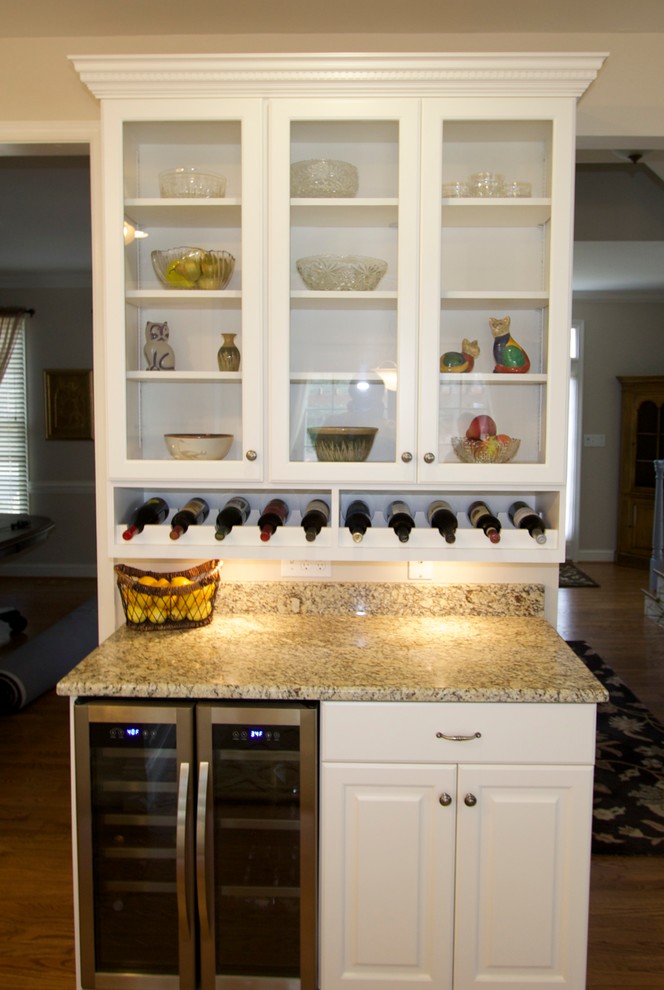 Inredning av ett klassiskt kök, med en undermonterad diskho, luckor med upphöjd panel, vita skåp, granitbänkskiva, rostfria vitvaror, mellanmörkt trägolv och en köksö
