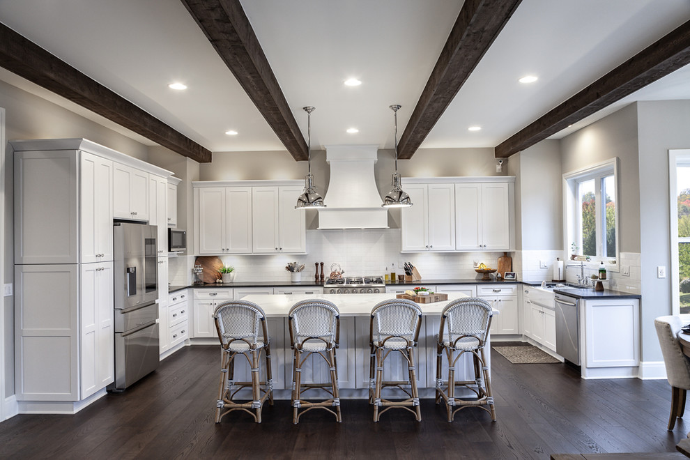 Inspiration for a transitional u-shaped medium tone wood floor and brown floor eat-in kitchen remodel in Detroit with a farmhouse sink, shaker cabinets, white cabinets, quartz countertops, white backsplash, subway tile backsplash, stainless steel appliances, an island and gray countertops