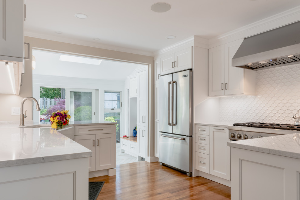 Example of a large transitional u-shaped medium tone wood floor and brown floor eat-in kitchen design in Boston with a farmhouse sink, shaker cabinets, white cabinets, quartzite countertops, white backsplash, ceramic backsplash, stainless steel appliances, a peninsula and white countertops